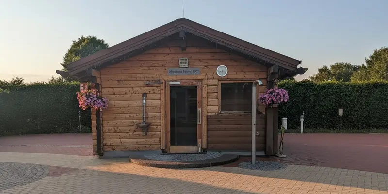Die Blockhaus-Sauna mit 100 Grad im Abendlicht, davor ein gepflasterter Platz